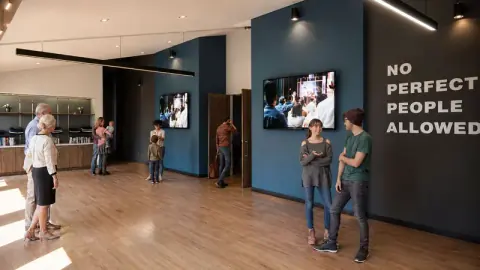 Architectural rendering of the lobby at 3D Community Church in Sanford, NC, with wood floors, wall-mounted screens and a "No Perfect People Allowed" feature wall, church interior design by Ossa Studio.
