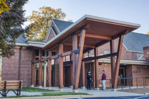Angled timber columns joined with black steel connections supporting the new entry canopy at Ascension Church in Charlotte, NC, seen in daylight, by Ossa Studio.