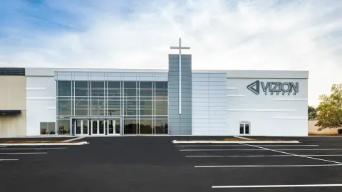 Renovated front elevation of Vizion Church in Charlotte, NC, with a glass curtain wall, metal-panel cross tower and new signage after the adaptive reuse project by Ossa Studio.