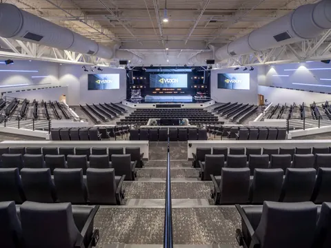 Looking down the center aisle of the tiered Vizion Church auditorium in Charlotte, NC, toward the stage and three video screens, a worship space by Ossa Studio.