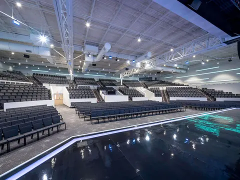 View from the lit stage edge across the seating sections of the Vizion Church auditorium in Charlotte, NC, with acoustic and lighting systems overhead, designed by Ossa Studio.