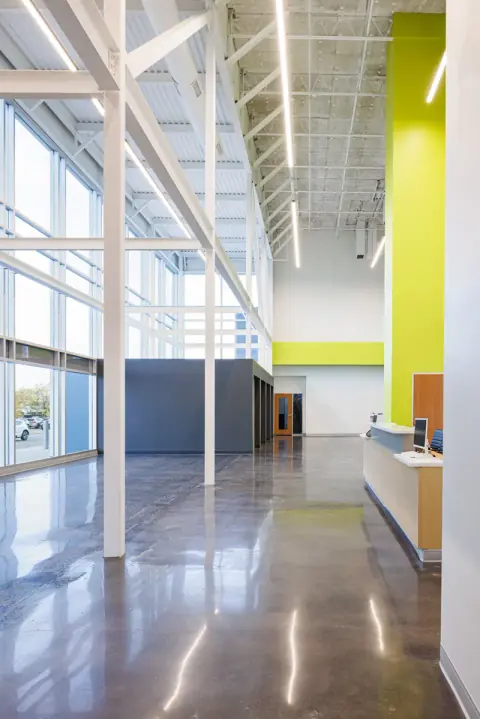Vertical view of the Vizion Church lobby in Charlotte, NC, with exposed white steel framing, linear lights and a lime-green column beside the reception desk, by Ossa Studio.