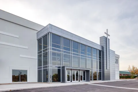 Daytime view of the glass curtain wall, covered entry doors and cross tower added to the Vizion Church façade in Charlotte, NC, by Ossa Studio.