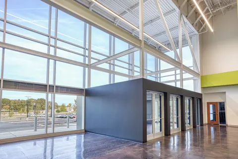 Tall glass wall, white steel framing and a dark entry vestibule with glass doors inside the Vizion Church lobby in Charlotte, NC, church interior architecture by Ossa Studio.