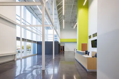 Double-height glass lobby with polished concrete floors, a lime-green accent wall and a welcome desk at Vizion Church in Charlotte, NC, a church renovation by Ossa Studio.