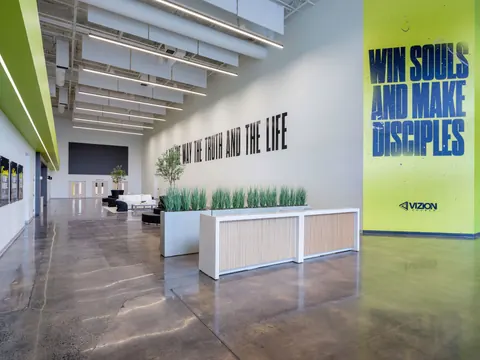 Lobby gathering area at Vizion Church in Charlotte, NC, with a slatted welcome desk, planters, lounge seating and large scripture graphics on the walls, designed by Ossa Studio.