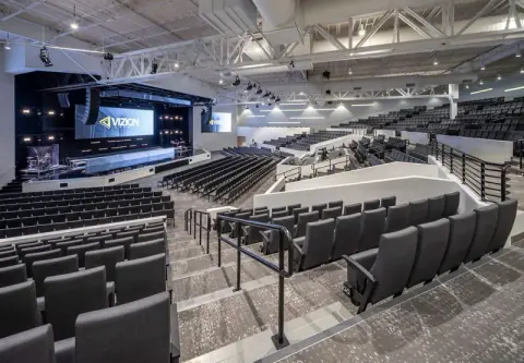 Side view of the Vizion Church auditorium in Charlotte, NC, showing stepped seating sections, railings and the stage, church interior architecture by Ossa Studio.